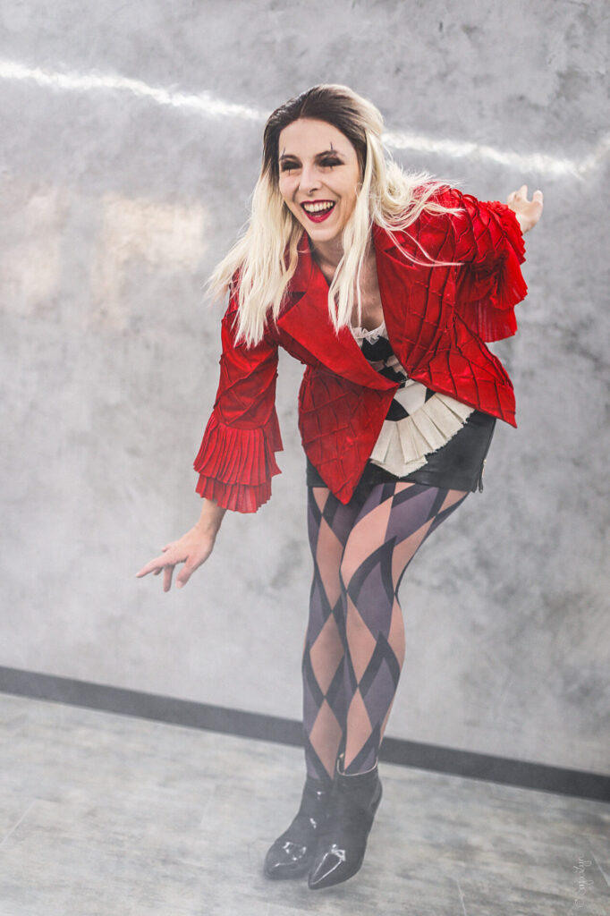 Cosplayer als Harley Quinn (Joker 2). Posiert stehend leicht nach vorne gebeugt und lachend.